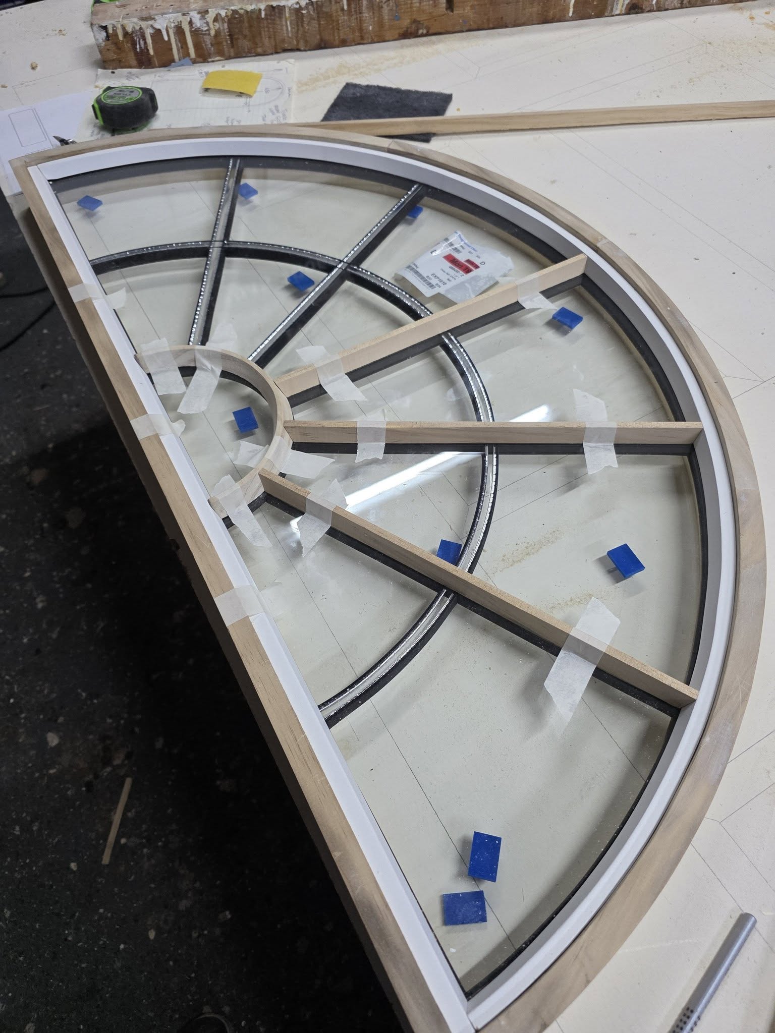 A quarter-round frame with its glass being glazed in on the bench