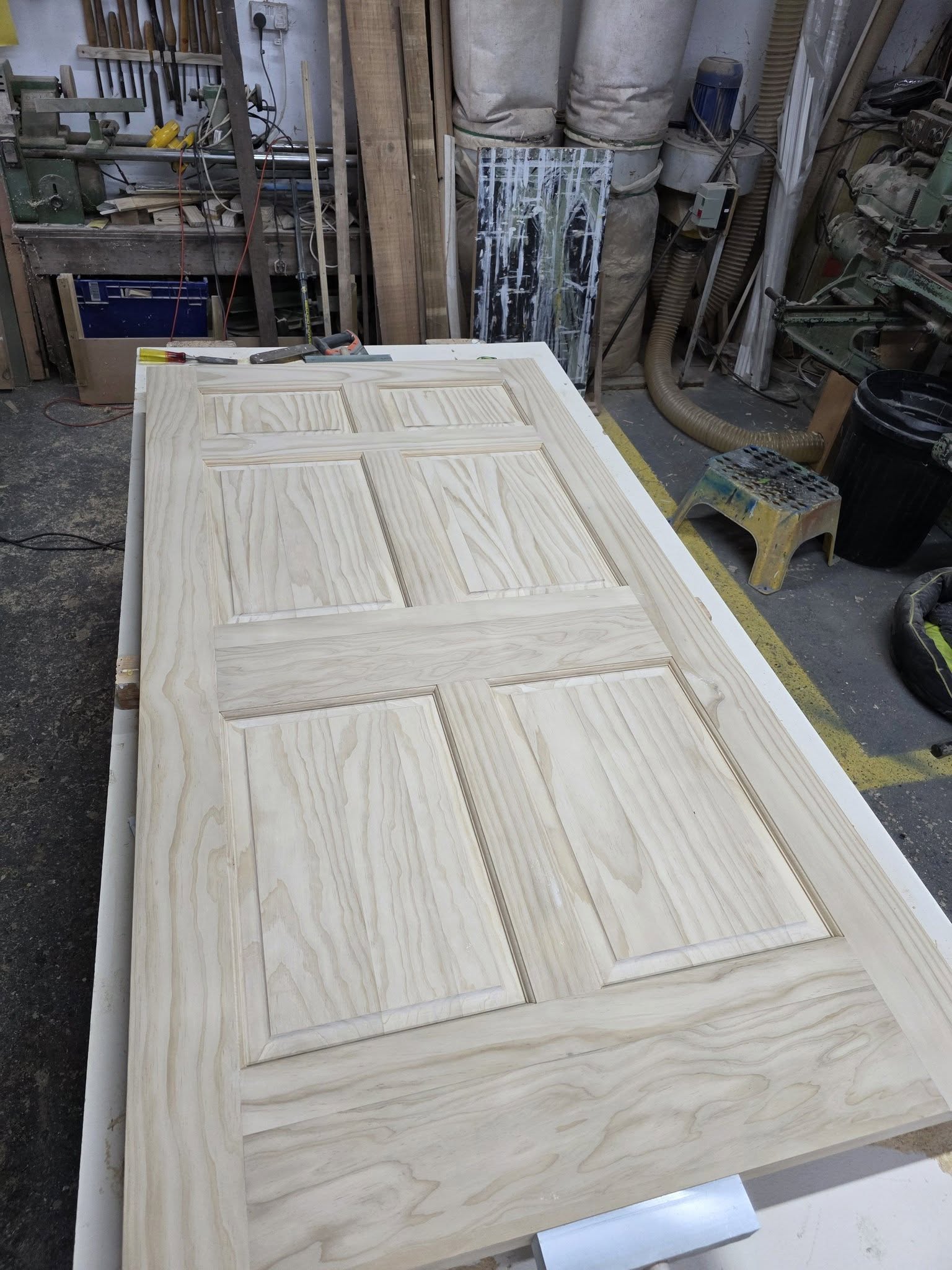 A six-panel timber door, made and sanded, on the workshop bench