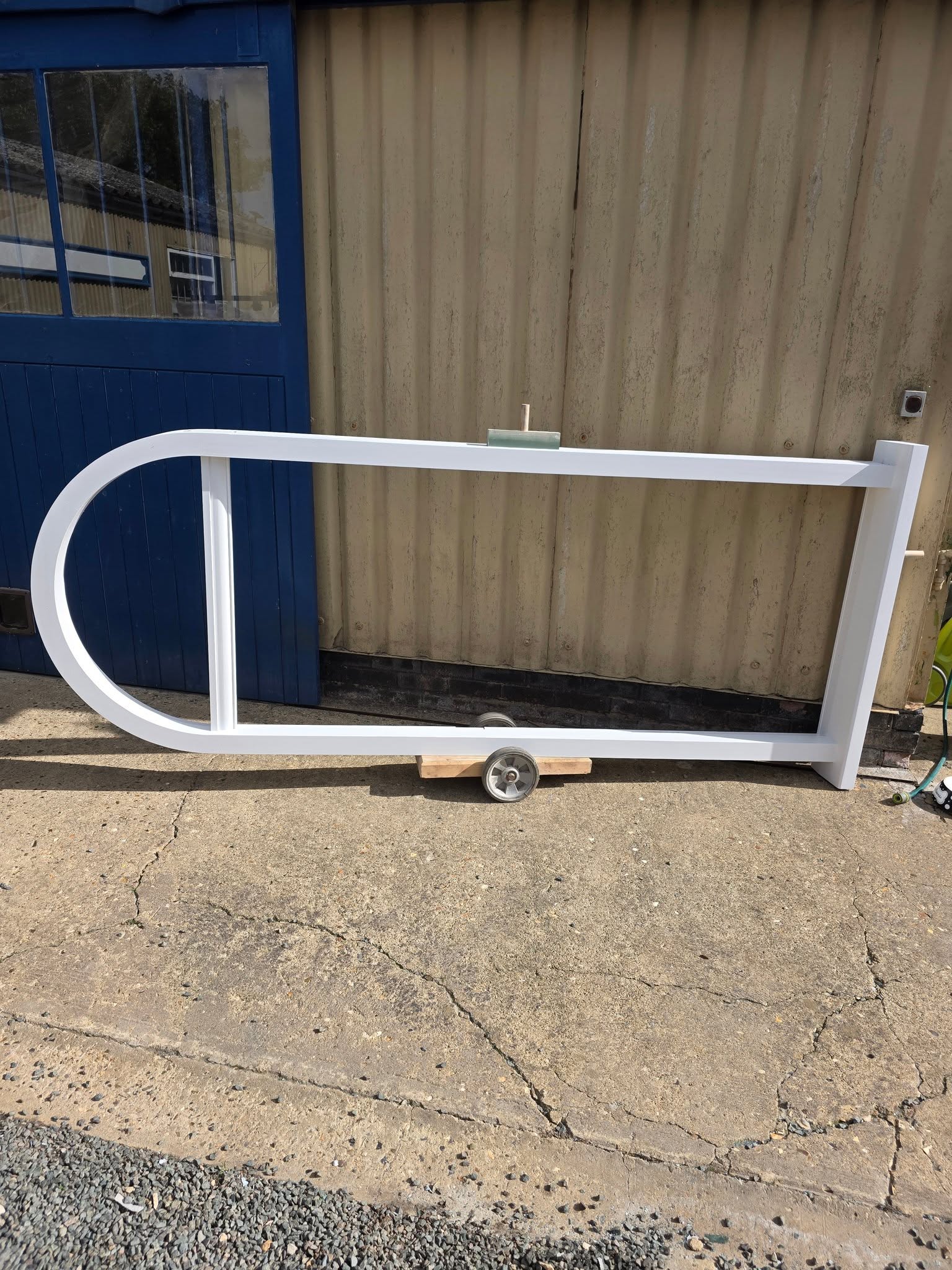 A long white painted frame with a curved end, outside the workshop
