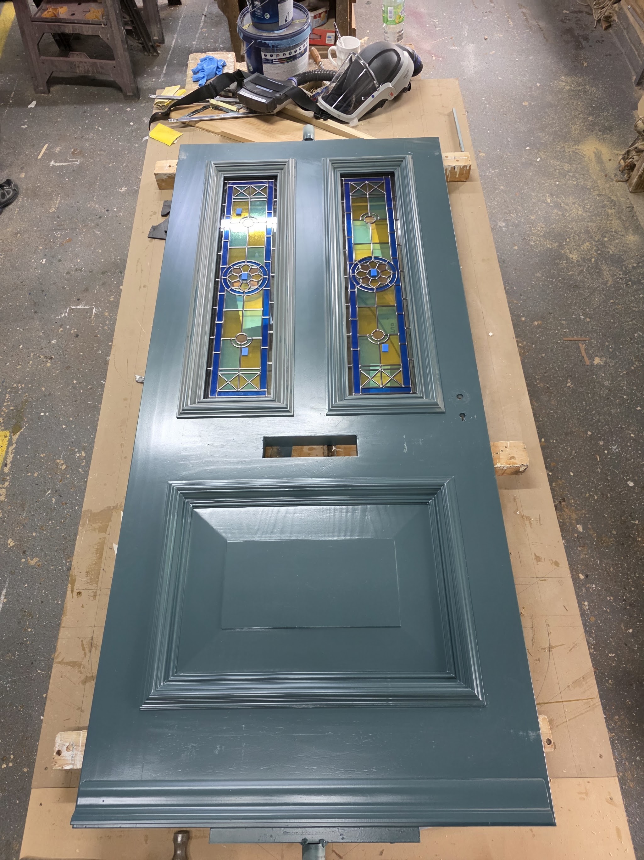 A blue-grey panelled front door with stained glass lights, finished on the bench